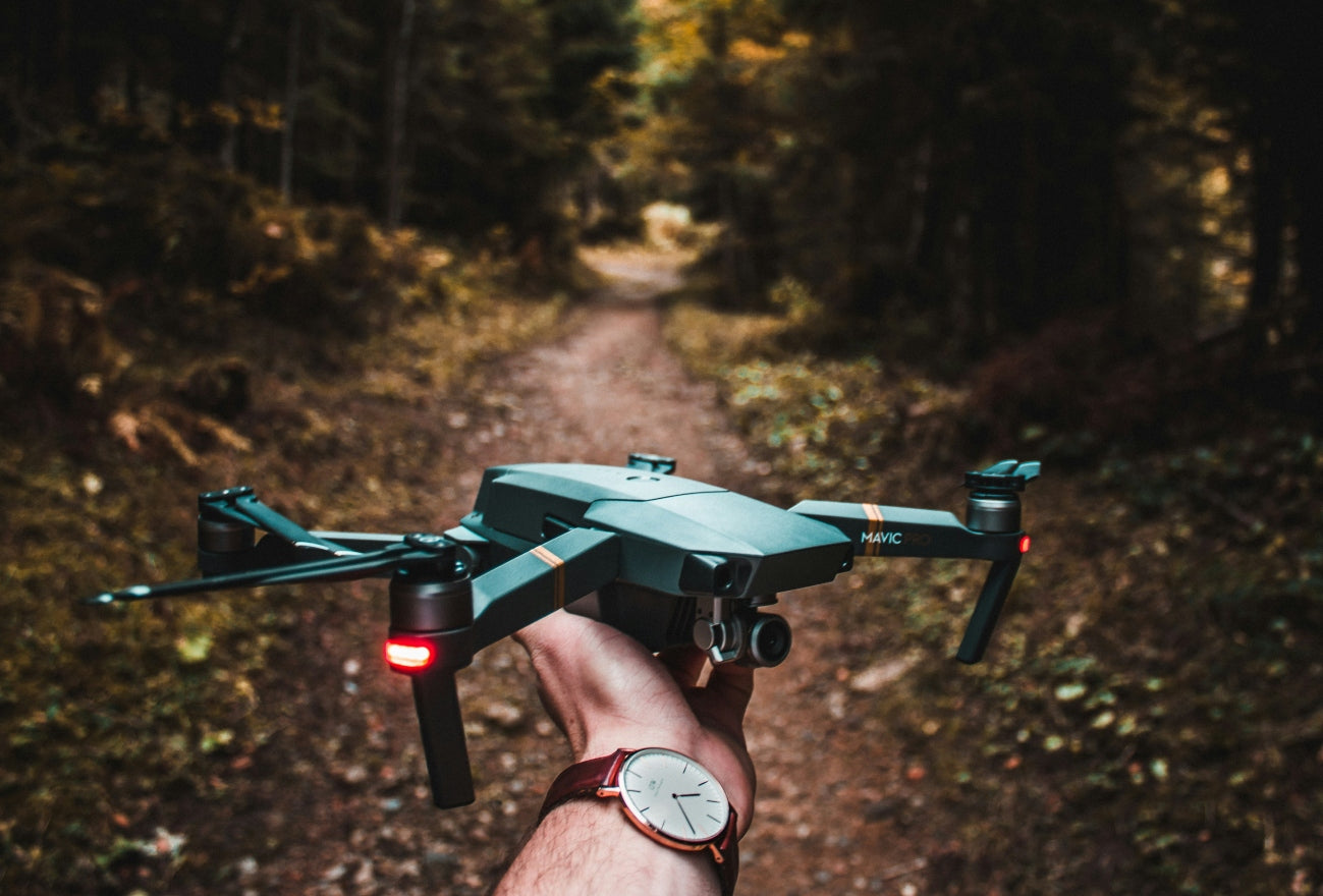 A person holding a DJI Mavic Pro drone with red lights glowing, ready for flight on a forest trail – Loft Shelf electronics gadgets.
