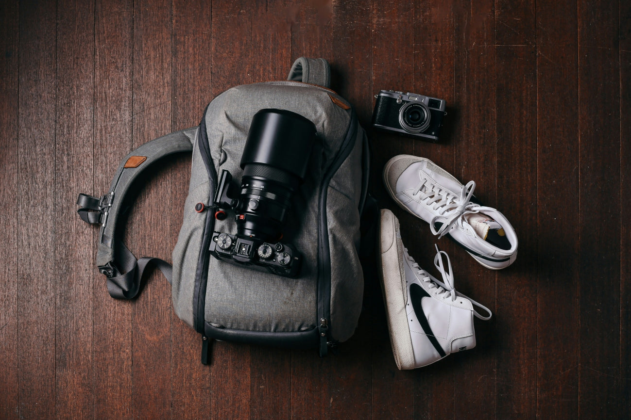Loft Shelf – Stylish flat lay featuring a gray camera backpack with a professional camera, vintage camera, and white Nike sneakers on a wooden floor.